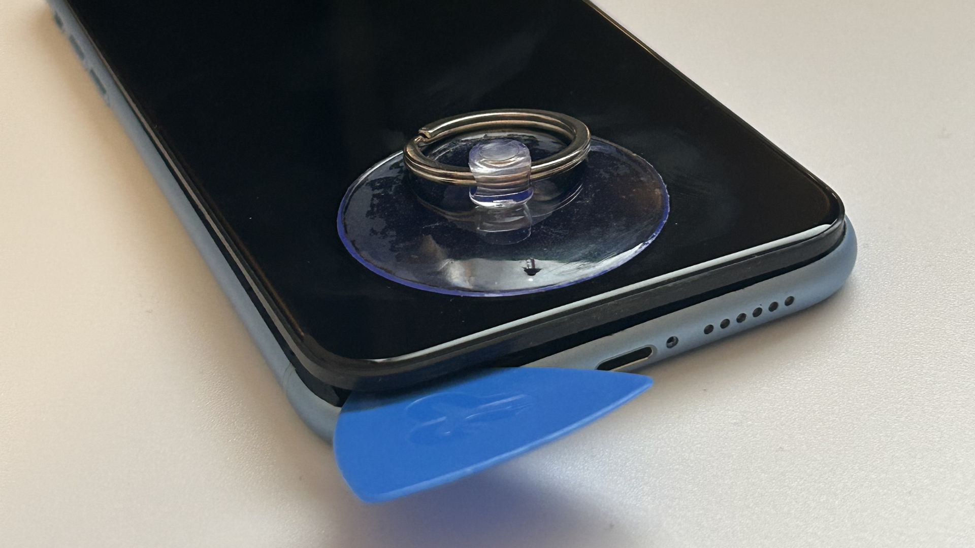 Close-up of the plastic pick wedged between the bottom-left corner of screen and chassis of device