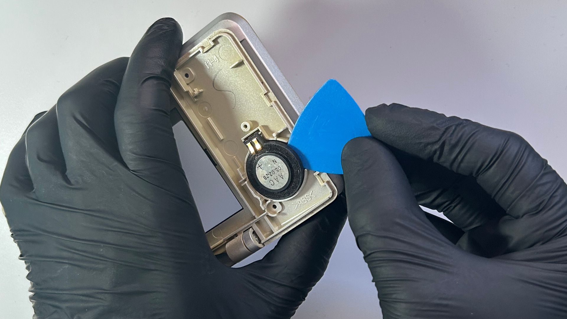 Plastic opening pick positioned underneath the second Nintendo DS speaker to remove it from the shell