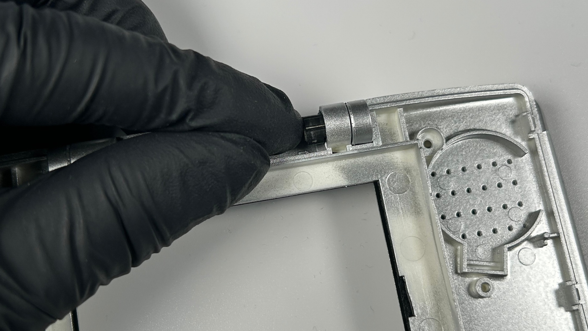 Installing the first black Nintendo DS hinge piece into the replacement shell