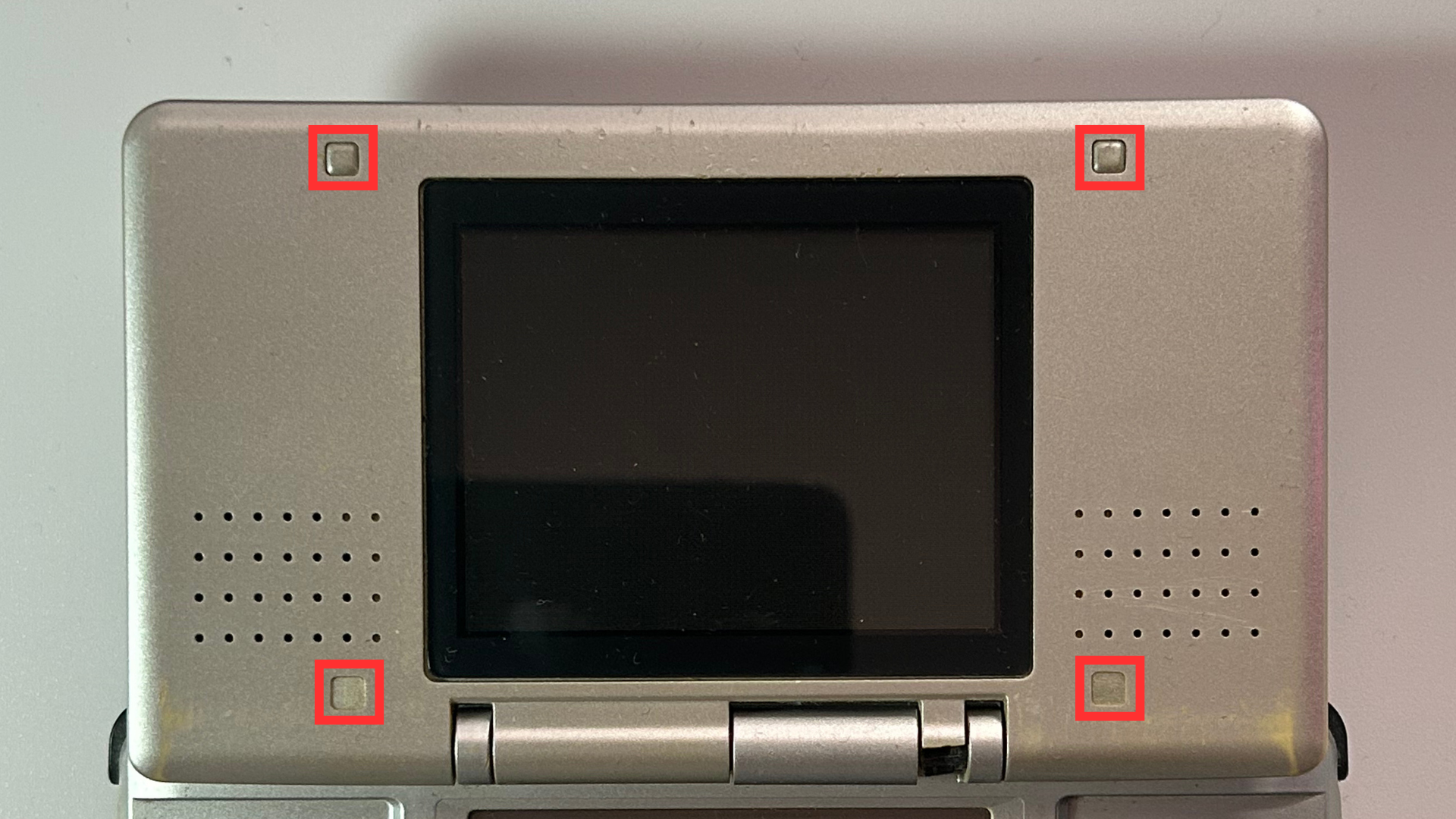 Original Nintendo DS showing the rubber screw covers around the top screen