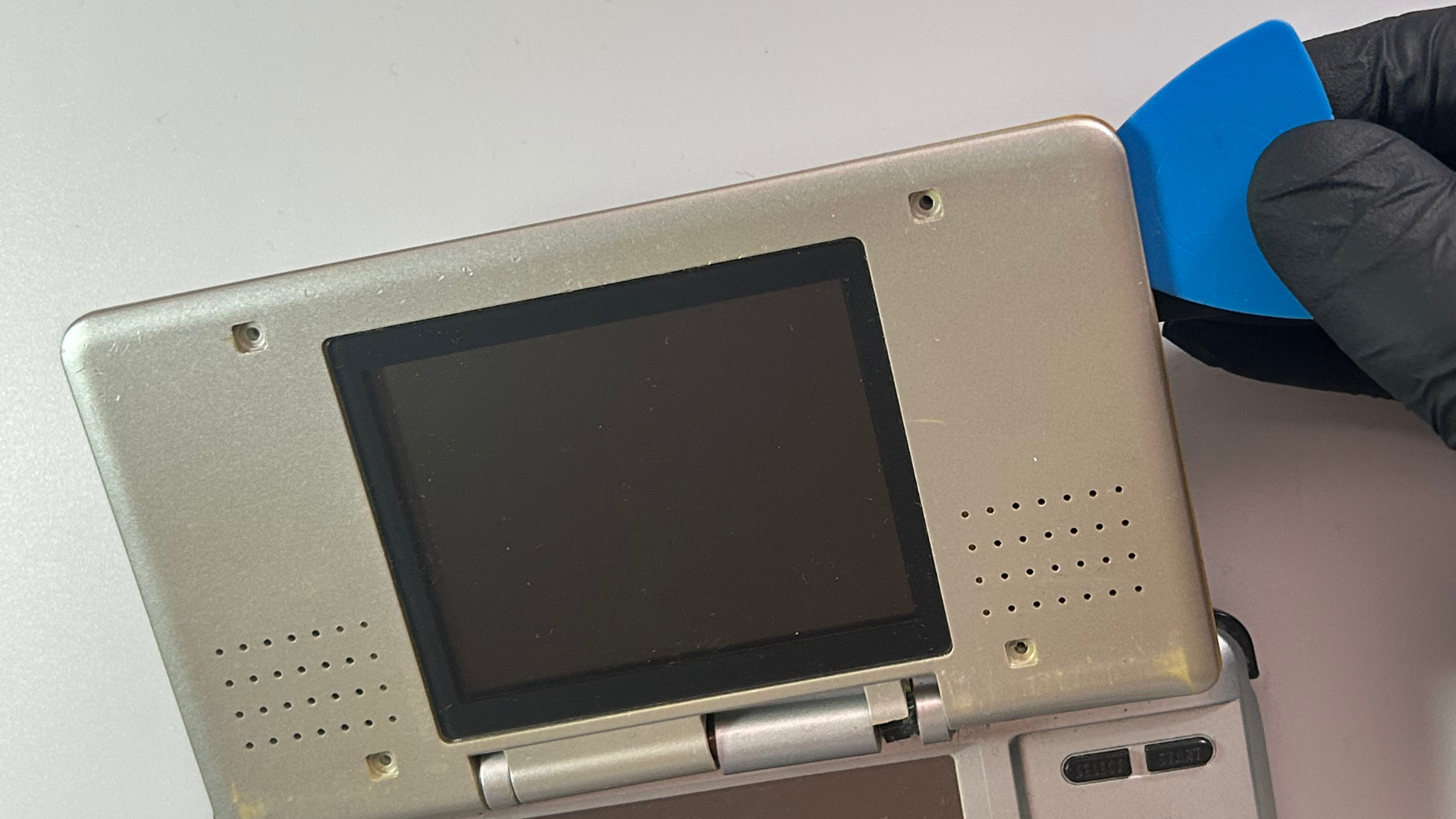 Plastic pry tool separating the rear section of the Nintendo DS upper screen housing