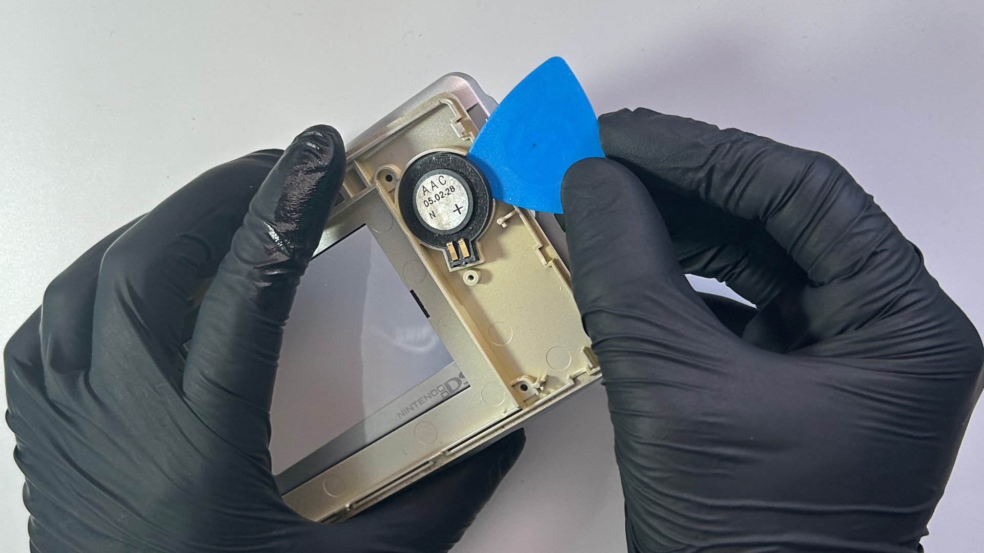 Original Nintendo DS speaker being carefully lifted from the upper screen housing