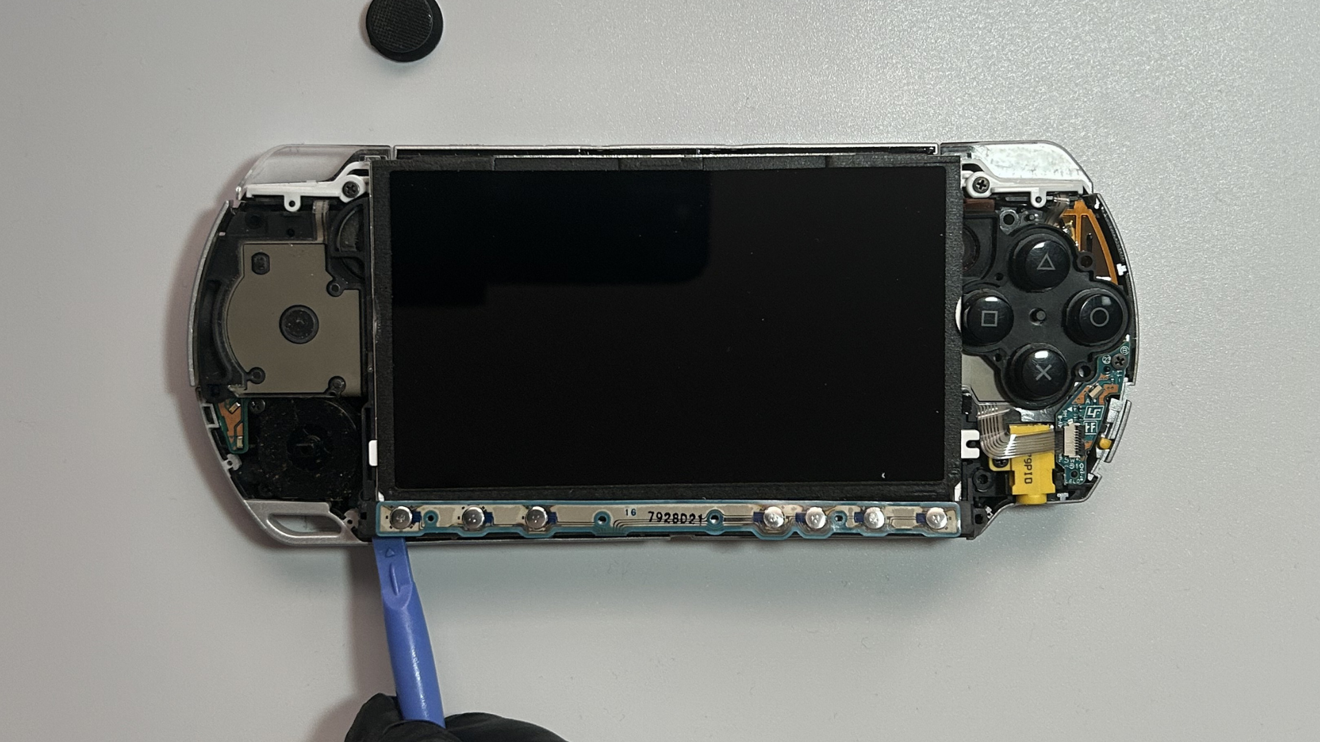 Plastic pry tool releasing one end of the PSP 2000 control button strip from the LCD